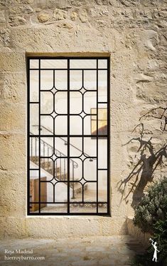 a window with bars on the side of a stone wall next to a potted plant