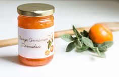 a jar of orange marmalade next to an orange plant and wooden utensils