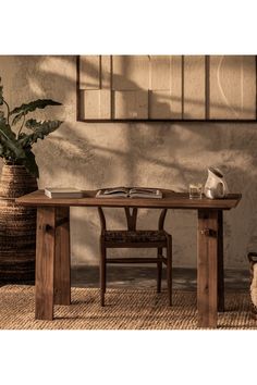 a wooden table with two chairs and a book on it in front of a potted plant