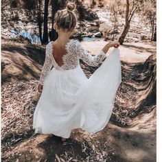 a woman in a white dress is walking through the woods with her back to the camera