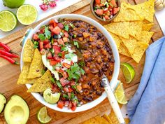 a white bowl filled with beans and salsa surrounded by tortilla chips, lime wedges and tomatoes