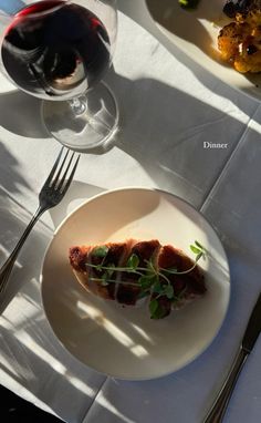 a white plate topped with food next to a glass of wine