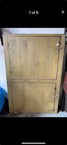 an old wooden cabinet with peeling paint on the doors and bottom panel, next to a blue plastic trash can