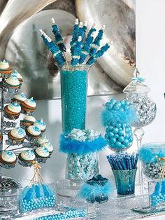 a table topped with blue and white cupcakes next to a vase filled with candy