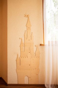 a wooden cutout of a castle on the wall next to a window with sheer curtains