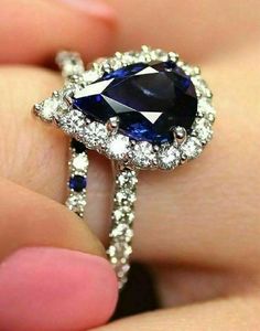 a woman's hand holding a ring with a blue stone and diamonds on it