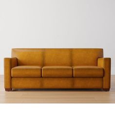 a brown leather couch sitting on top of a hard wood floor next to a white wall