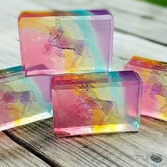 three soap bars sitting on top of a wooden table covered in multicolored liquid