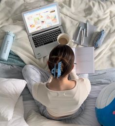 a woman sitting on top of a bed next to a laptop computer and other items