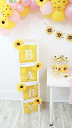 a baby shower party with sunflowers and balloons on the wall, cake table