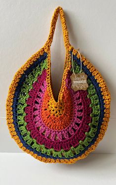 a multicolored crocheted bag hanging on the wall with a tag attached to it