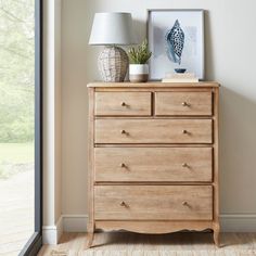 a wooden dresser sitting next to a window with a lamp and pictures on top of it