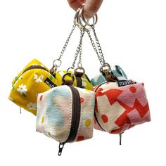 four small purses hanging from chains on a white background with one being held by a person's hand