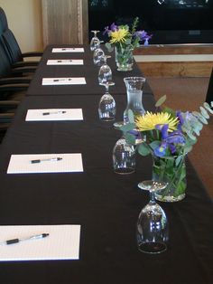 a long table with several vases filled with flowers and writing paper on top of it