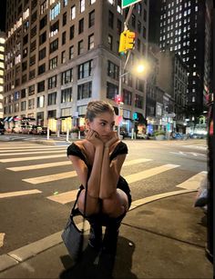 a woman sitting on the side of a street next to a traffic light at night