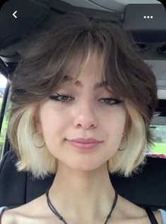 a woman with short blonde hair sitting in a car looking at the camera and smiling