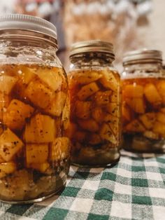 three jars filled with food sitting on top of a table covered in checkered cloth