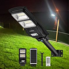 the solar powered street light is on top of some green grass and has two remote controls