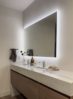 a bathroom vanity with two sinks and a large mirror above it that is illuminated by lights