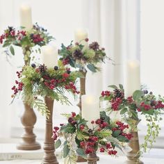 three tall wooden candlesticks decorated with greenery, berries and pineconis