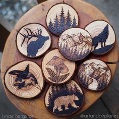 six wood burned coasters with animals and trees on them, sitting on a wooden table