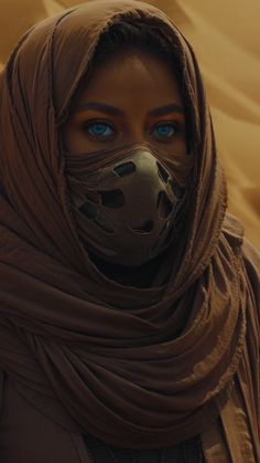 a woman with blue eyes wearing a brown scarf and covering her face is looking at the camera