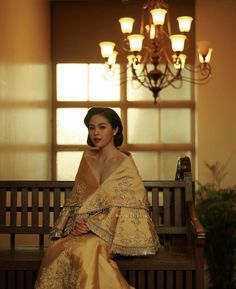 a woman sitting on top of a wooden bench next to a light chandelier