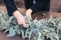 a person arranging flowers on top of a table with leaves and twigs around it,