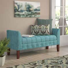 a blue bench sitting in front of a window next to a rug and potted plant