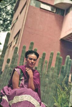 a woman sitting on top of a bench in front of a cactus tree and building