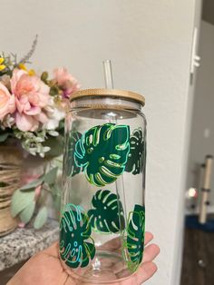 a hand holding a glass with green leaves on it