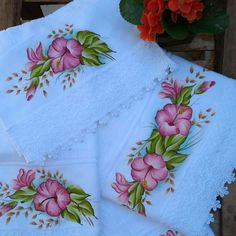 four white handkerchiefs with pink flowers and green leaves on them, sitting next to a potted plant