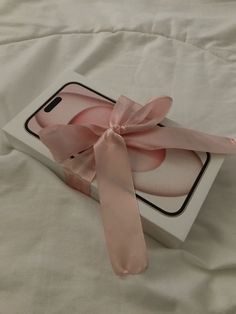 an open box with a pink ribbon tied around it on top of a white sheet