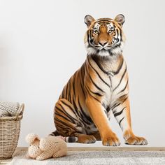 a large tiger sitting on top of a rug next to a basket and stuffed animal