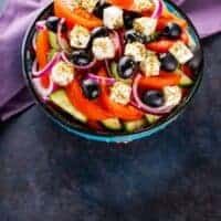 a bowl filled with assorted veggies on top of a black table next to a purple napkin