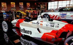 a racing car is on display in a showroom with other cars and trucks behind it