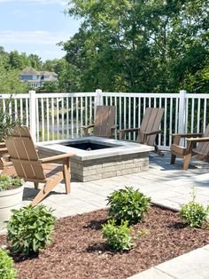 an outdoor fire pit surrounded by lawn chairs and landscaping plants on a patio with white picket fence