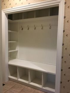 an empty white closet with shelves and hooks on the wall next to a tiled floor