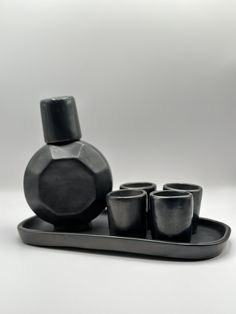 an assortment of black cups and vases on a tray