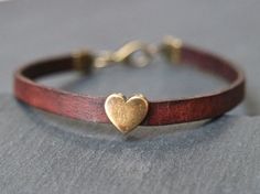 a leather bracelet with a gold heart charm on it's end, sitting on a gray surface