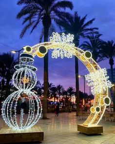 an outdoor sculpture with lights on it and palm trees in the background at night time