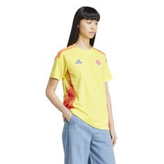 a young woman wearing a yellow shirt and blue jeans stands in front of a white background