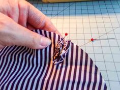 a person is working on a piece of fabric with pins and thread in the background