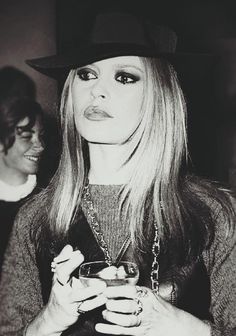 black and white photograph of a woman with long hair wearing a hat holding a drink