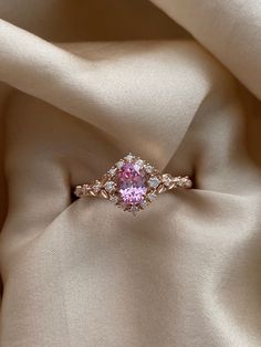 a pink diamond ring sitting on top of a white cloth covered in satin material,