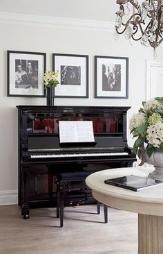 there is a piano in the living room with pictures on the wall behind it and a chandelier hanging from the ceiling