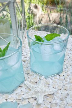 two glasses filled with ice and mint sitting on a table next to a starfish