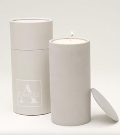 a white candle sitting next to a canister on a white surface with the lid open