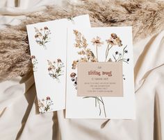 two greeting cards with wildflowers on them sitting on a white bed sheet in front of a furry pillow