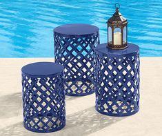 three blue stools sitting next to a pool with a lantern on one side and a candle holder on the other